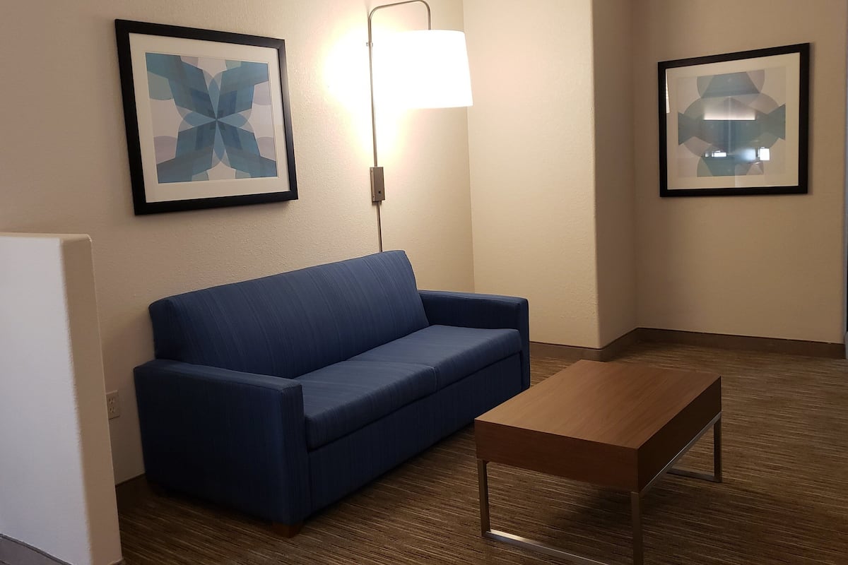 A hotel room with a blue sofa, a wooden coffee table, and two framed abstract artworks on the wall.