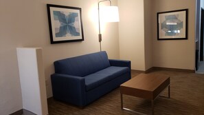A hotel room with a blue sofa, a wooden coffee table, and two framed abstract artworks on the wall. - Holiday Inn Express Hotel & Suites Weslaco by IHG (Weslaco)