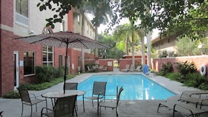 A swimming pool with lounge chairs and an umbrella, surrounded by brick buildings and greenery. - Holiday Inn Express Hotel & Suites Weslaco by IHG (Weslaco)