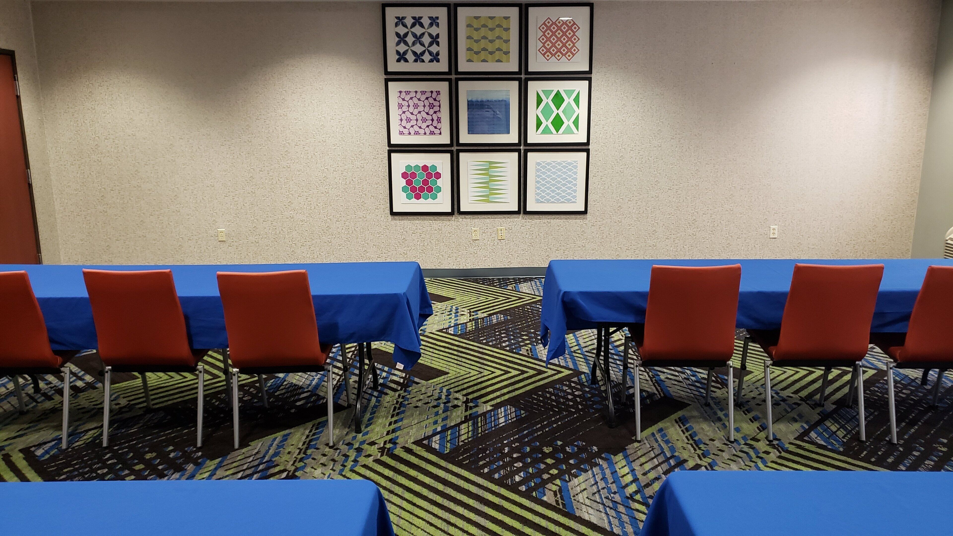 A conference room with tables covered in blue tablecloths, red chairs, and patterned carpet.