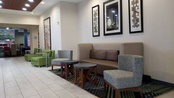 A lobby with a sofa, chairs, and tables, and a wall with framed artwork.