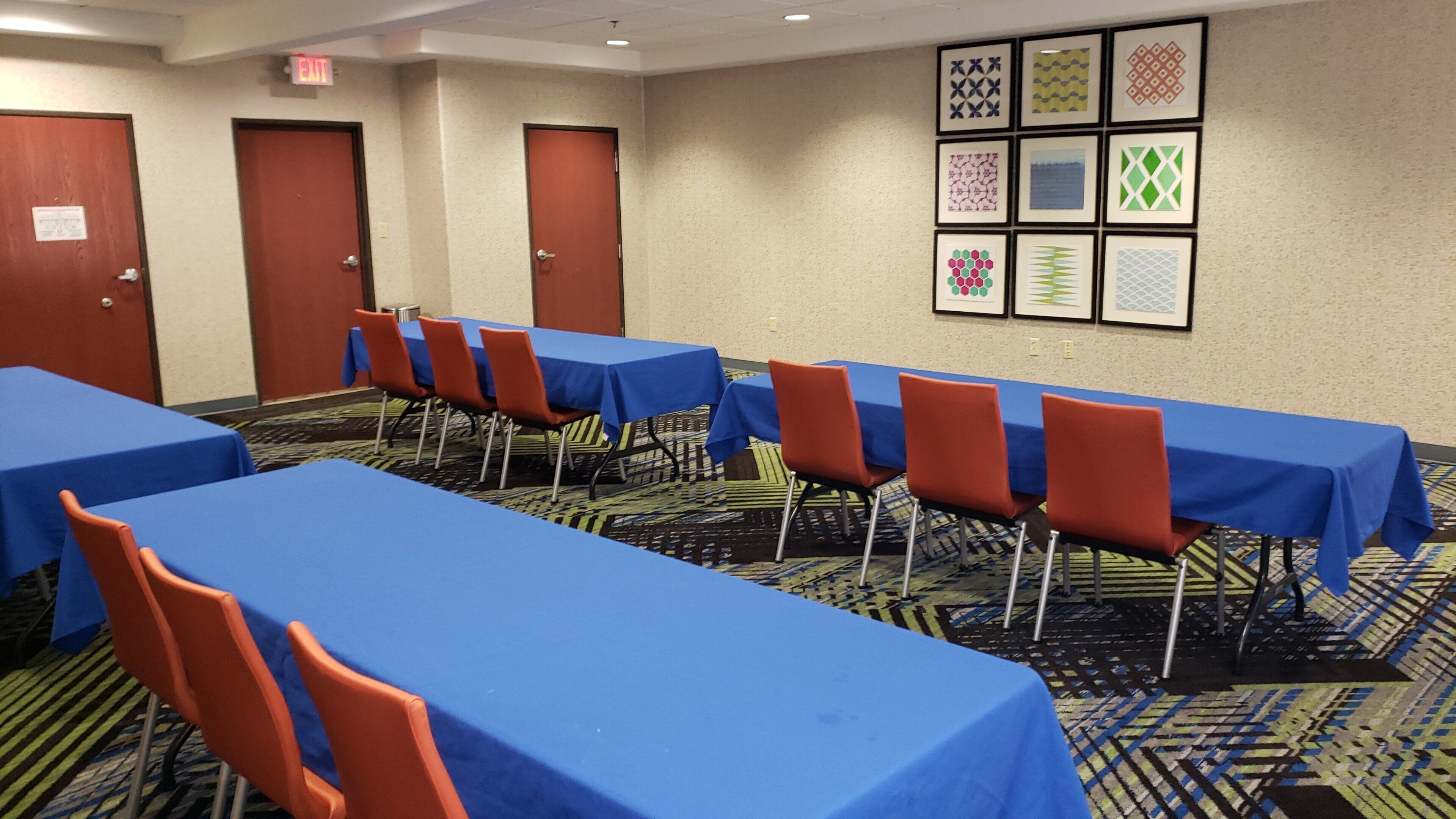 A conference room with multiple tables and chairs, carpeted floor, and framed artwork on the wall.