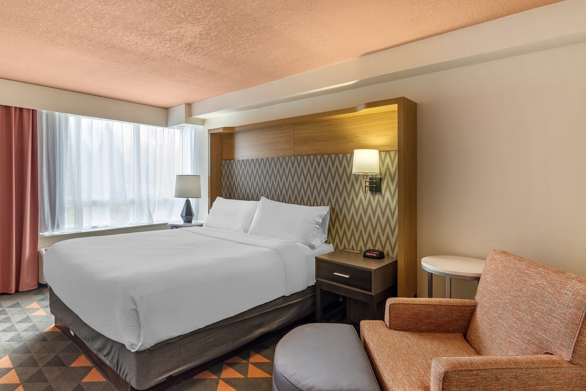 A hotel room with a large bed, a nightstand with a lamp, a small table, and a sofa.