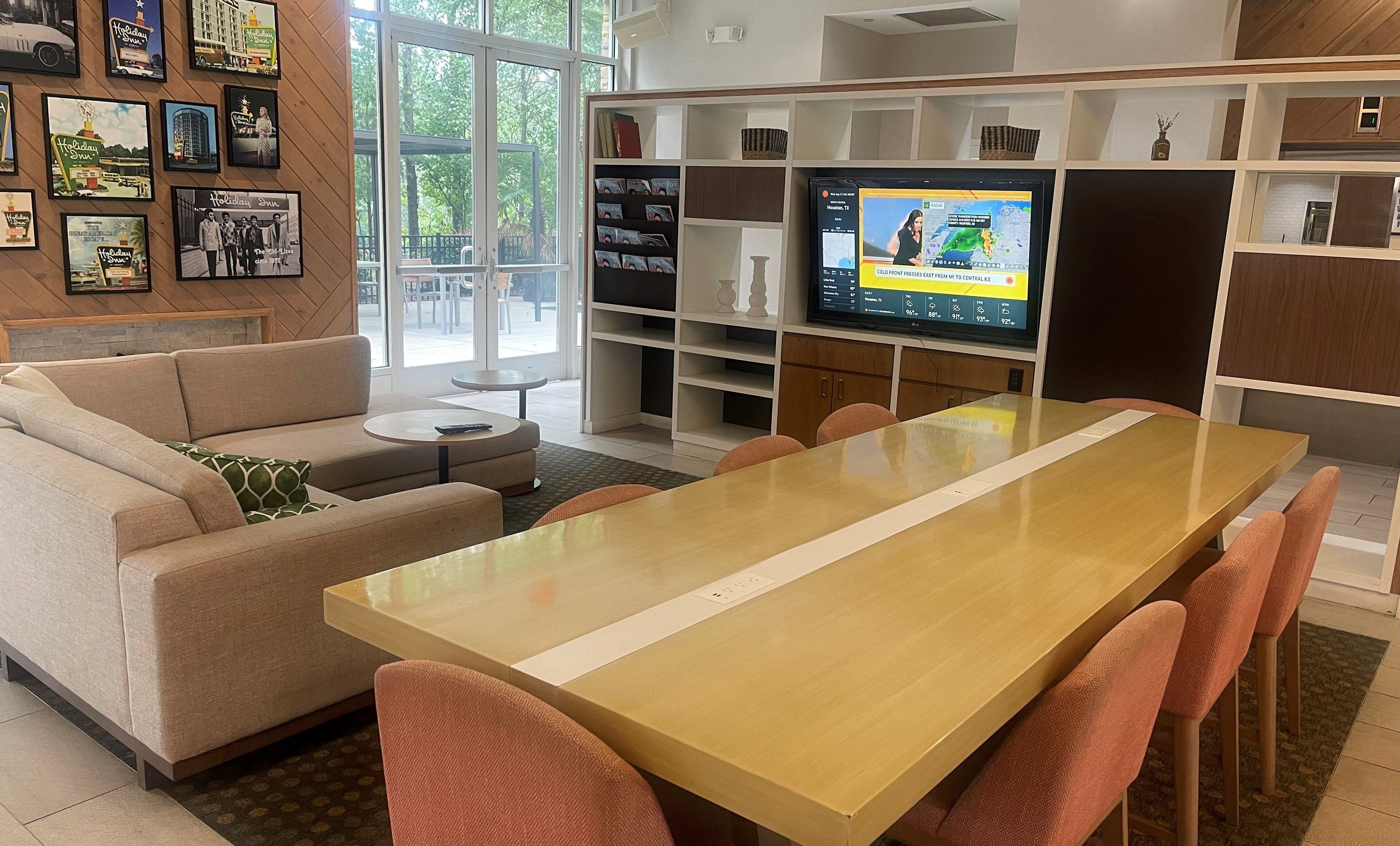 A modern living room with a sofa, coffee table, and a dining table with chairs. There is a television on a stand with a map display.