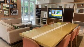 A modern living room with a sofa, coffee table, and a dining table with chairs. There is a television on a stand with a map display.