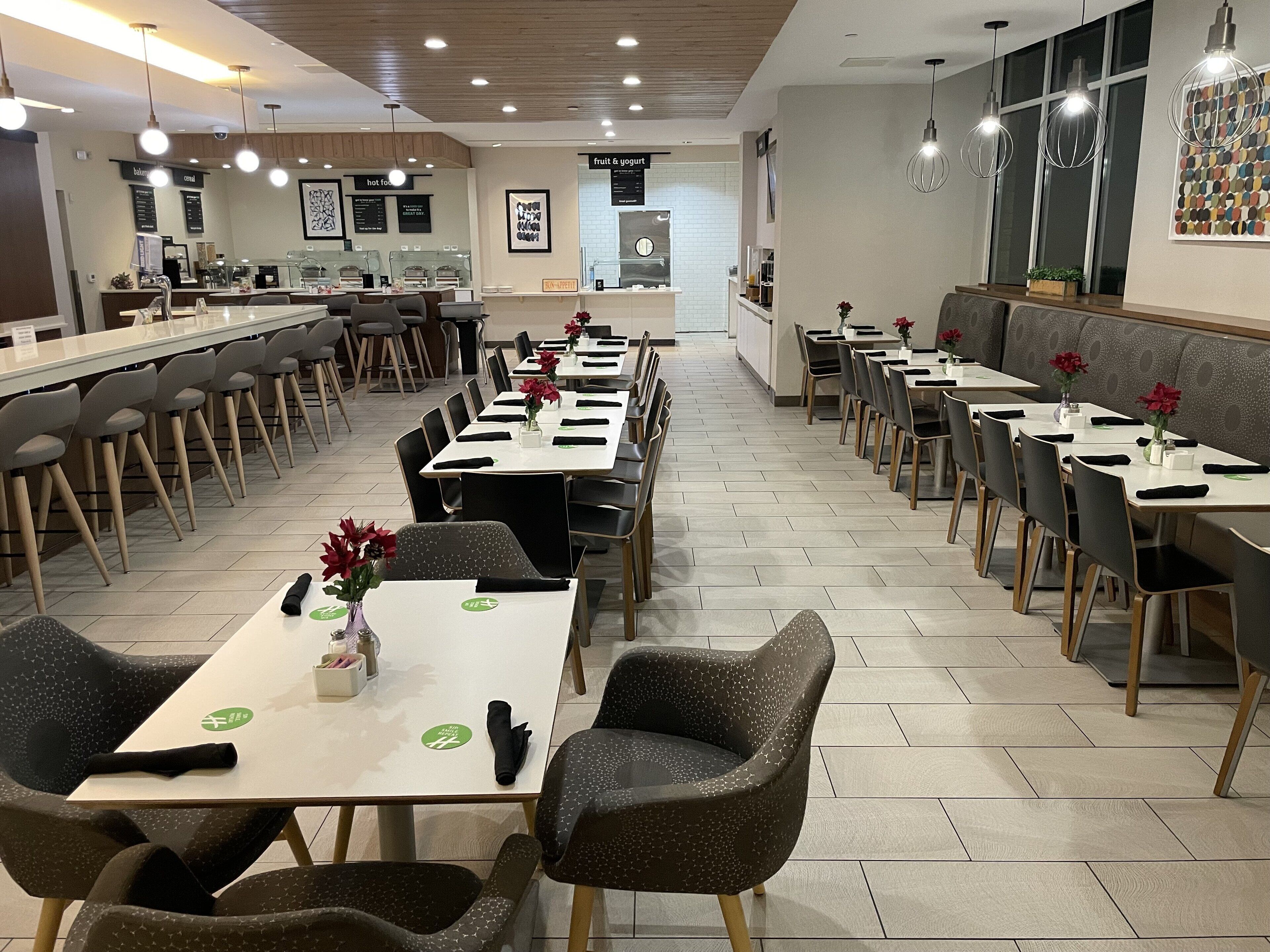 Un restaurante moderno con mesas comunitarias largas y cabinas, que presenta un diseño contemporáneo y limpio con detalles de madera y piso de baldosas.