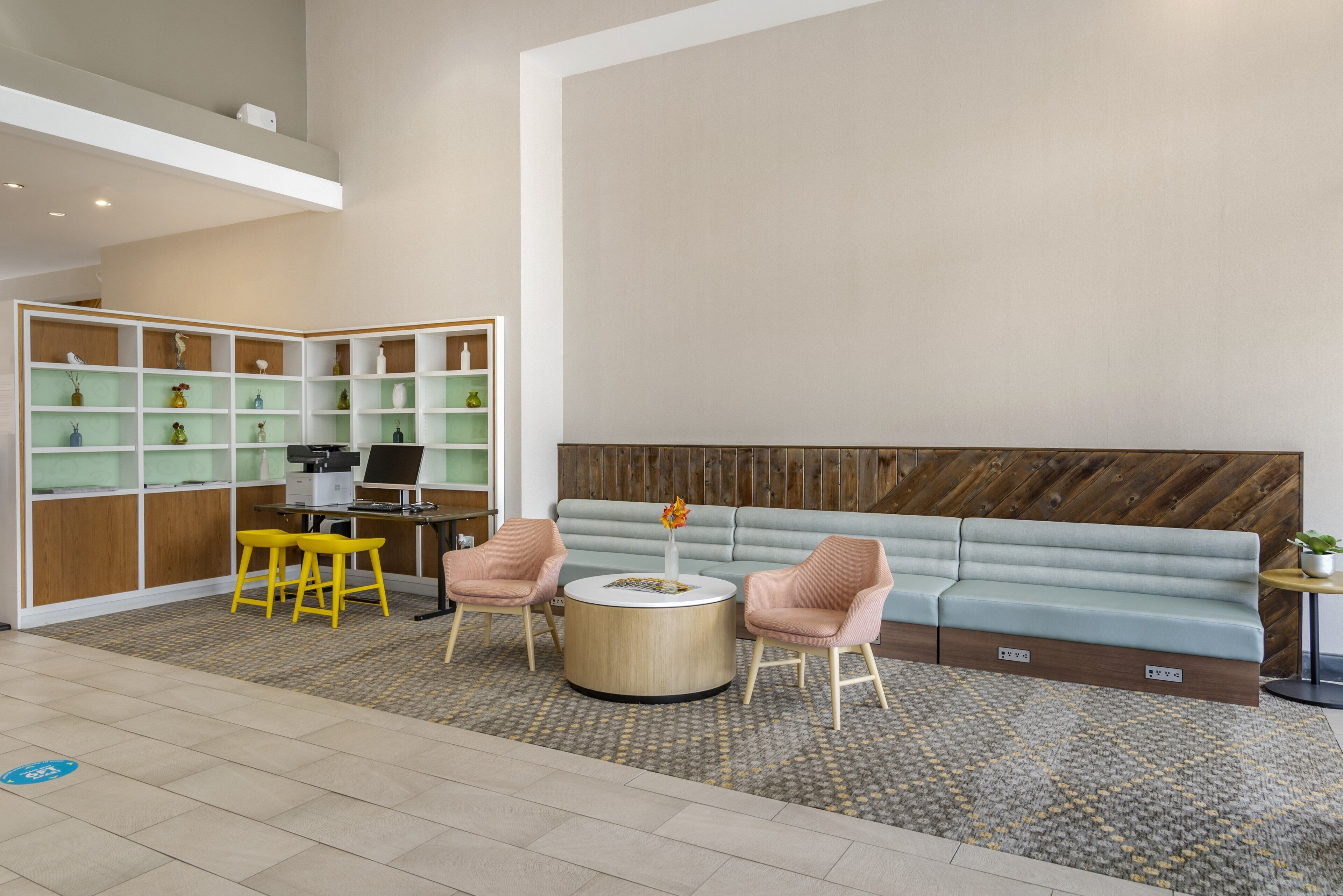A modern lobby with a seating area, a reception desk, and a shelving unit with various items.
