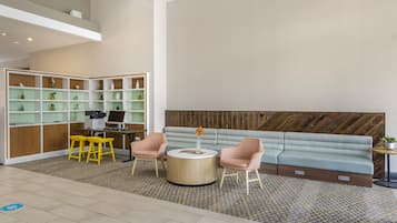 A modern lobby with a seating area, a reception desk, and a shelving unit with various items.
