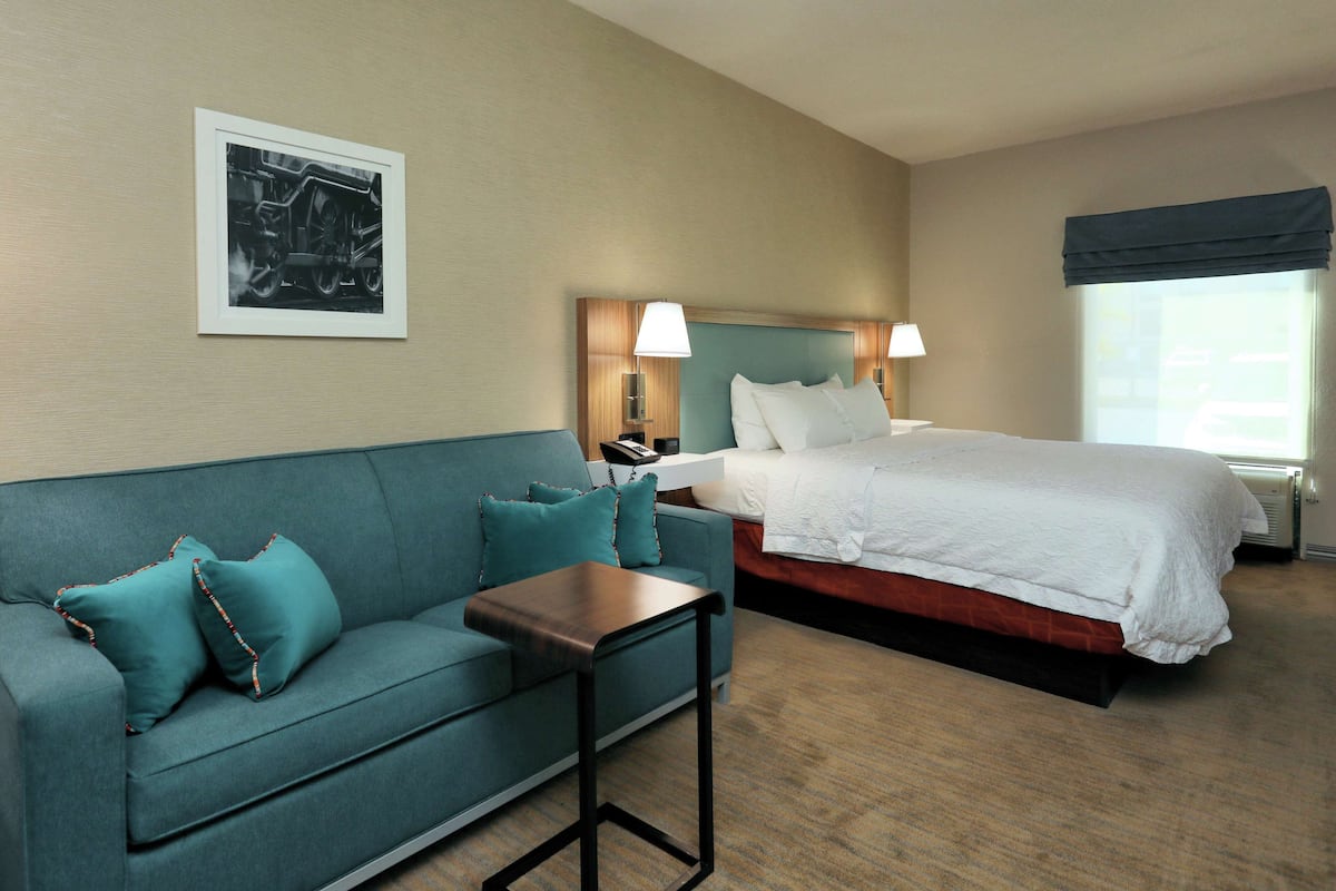 Una camera d'albergo con un letto, una poltrona, un tavolino e un quadro appeso al muro.