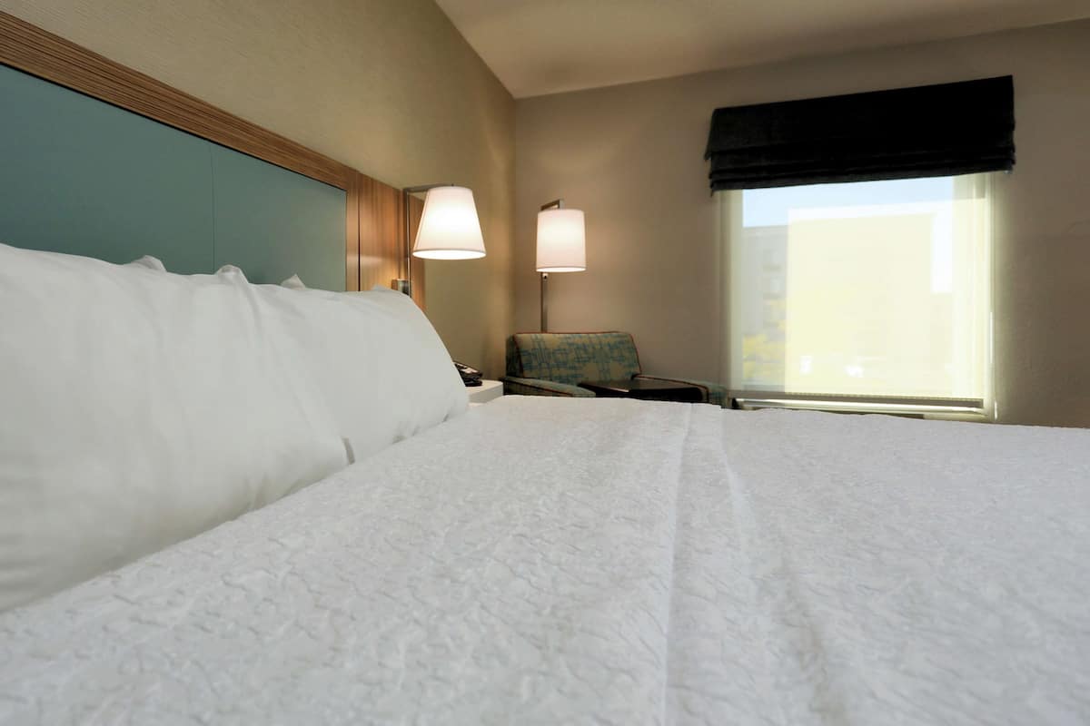 Una camera d'albergo con un letto grande, due lampade ai comodini, una sedia e una finestra con tende.