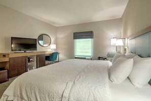 A hotel room with a large bed, a desk with a television, a chair, a window with a view, and a nightstand with lamps.