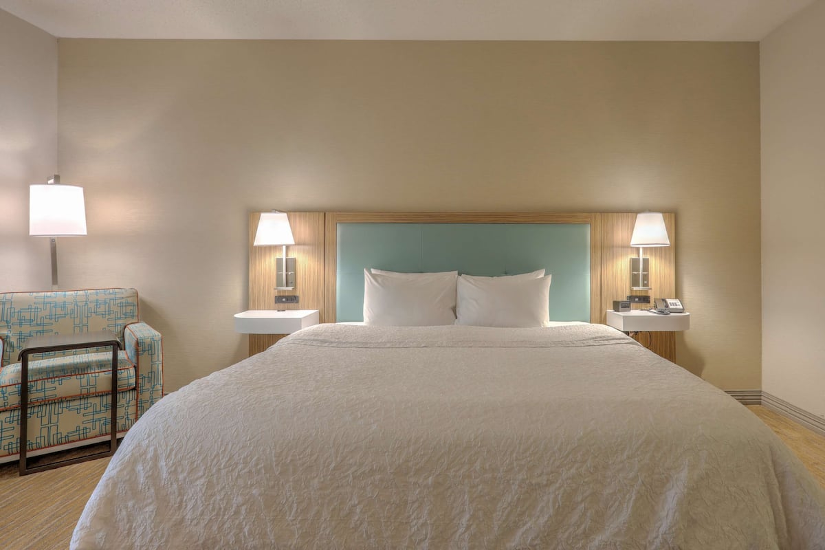 Una camera d'albergo con un letto grande, due comodini con lampade, una sedia e una testiera in legno.