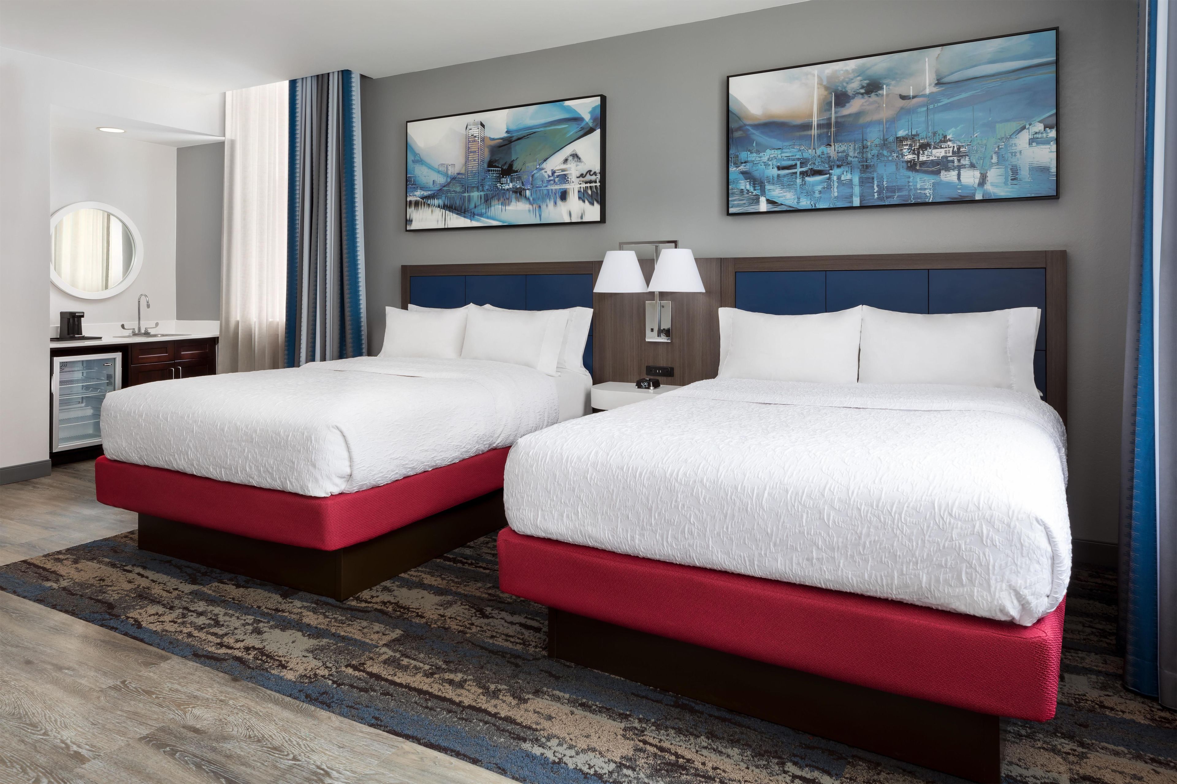 A hotel room with two beds, a nightstand, a mirror, and artwork on the walls.