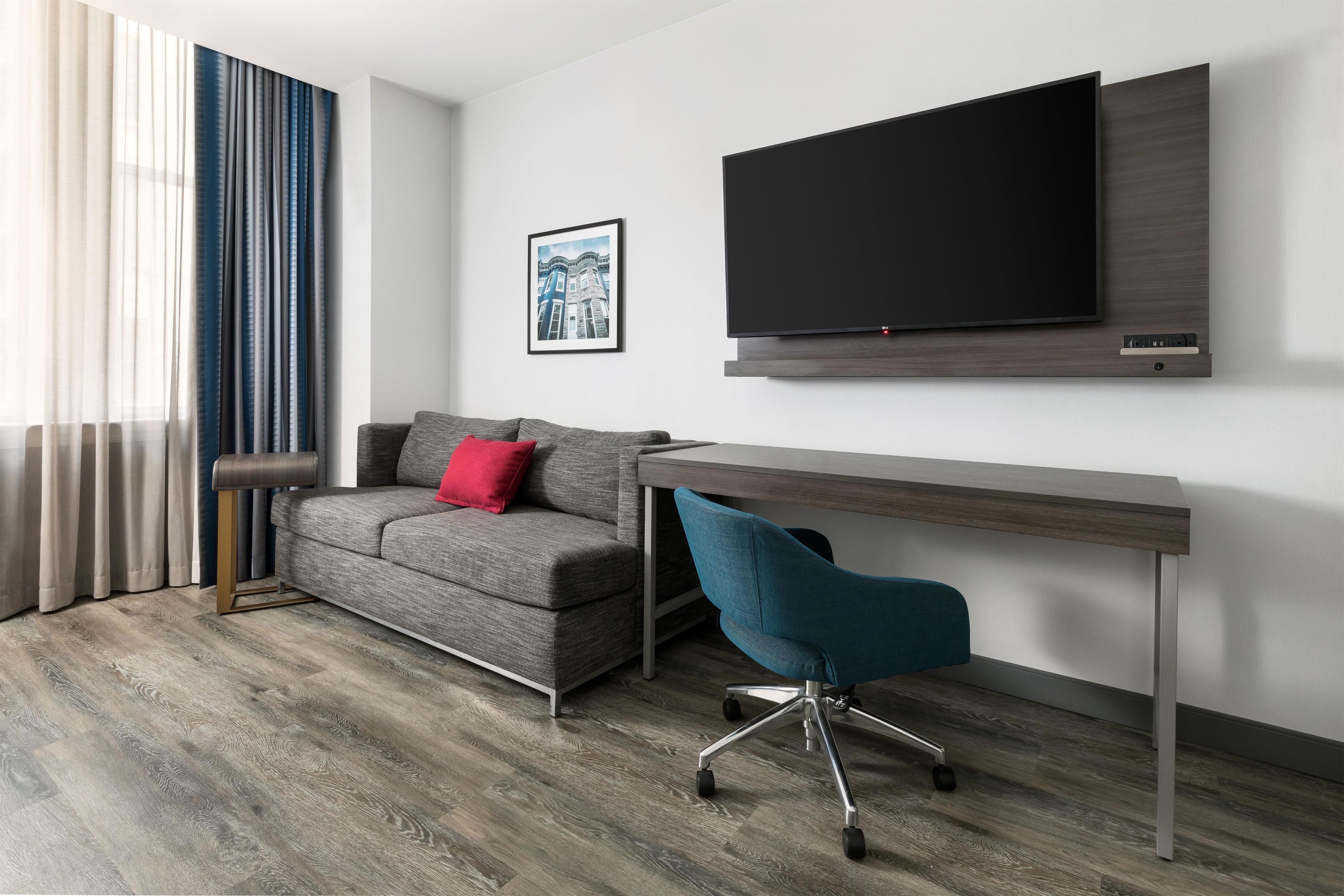 Una sala de estar moderna con un sofá gris, una silla de oficina turquesa, un televisor de pantalla plana montado en la pared y un cuadro enmarcado encima del televisor.