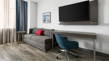 Una sala de estar moderna con un sofá gris, una silla de oficina turquesa, un televisor de pantalla plana montado en la pared y un cuadro enmarcado encima del televisor.