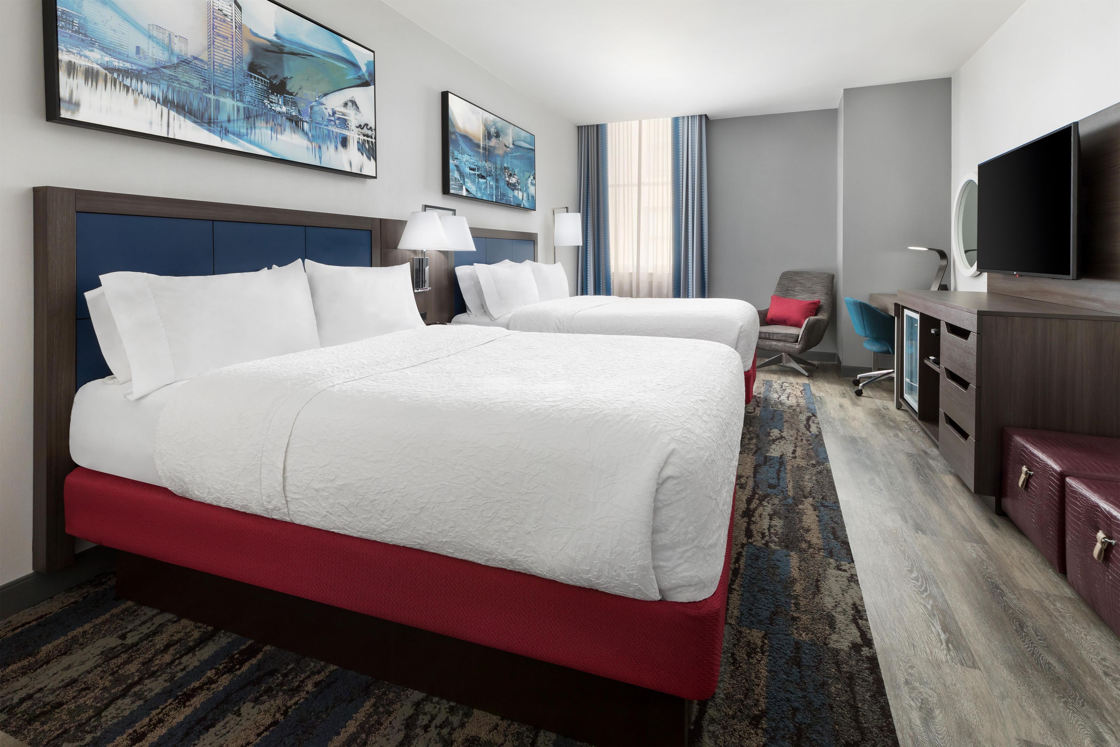 A hotel room with a large bed, a desk, a chair, a TV, and artwork on the walls.
