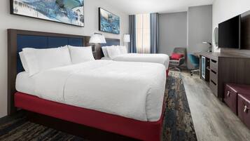 A hotel room with a large bed, a desk, a chair, a TV, and artwork on the walls.