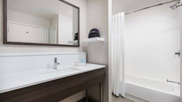 Une salle de bain avec un lavabo blanc, un miroir, un rideau de douche et un porte-serviettes.