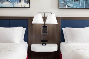 Une chambre d’hôtel avec deux lits, une table de chevet dotée d’une horloge numérique et un luminaire fixé au mur.