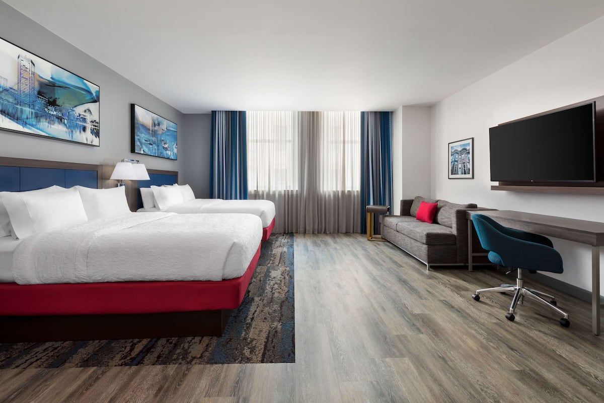 Ein Hotelzimmer mit zwei Betten, einem Schreibtisch, einem Sessel, einem Fernseher und Bildern an den Wänden.