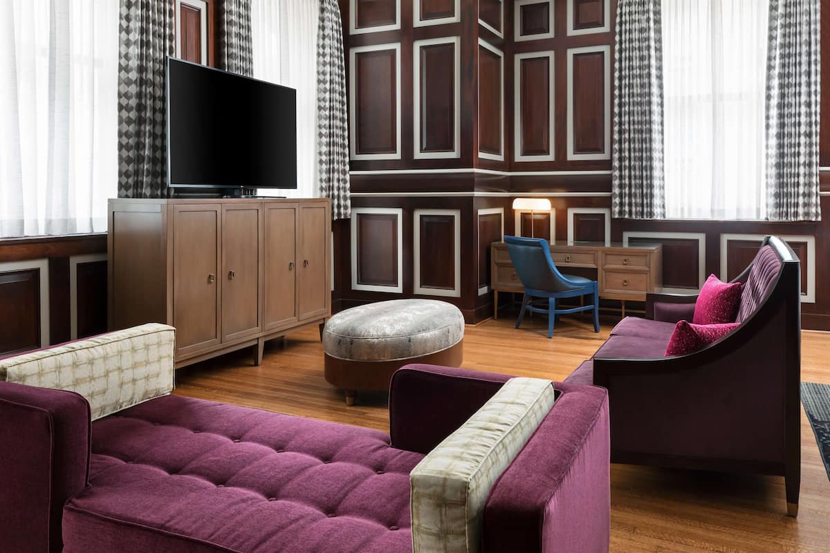 Ein modernes Wohnzimmer mit Flachbildfernseher, einer Couch, einem Sessel, einem Schreibtisch und einer Wand mit Muster.
