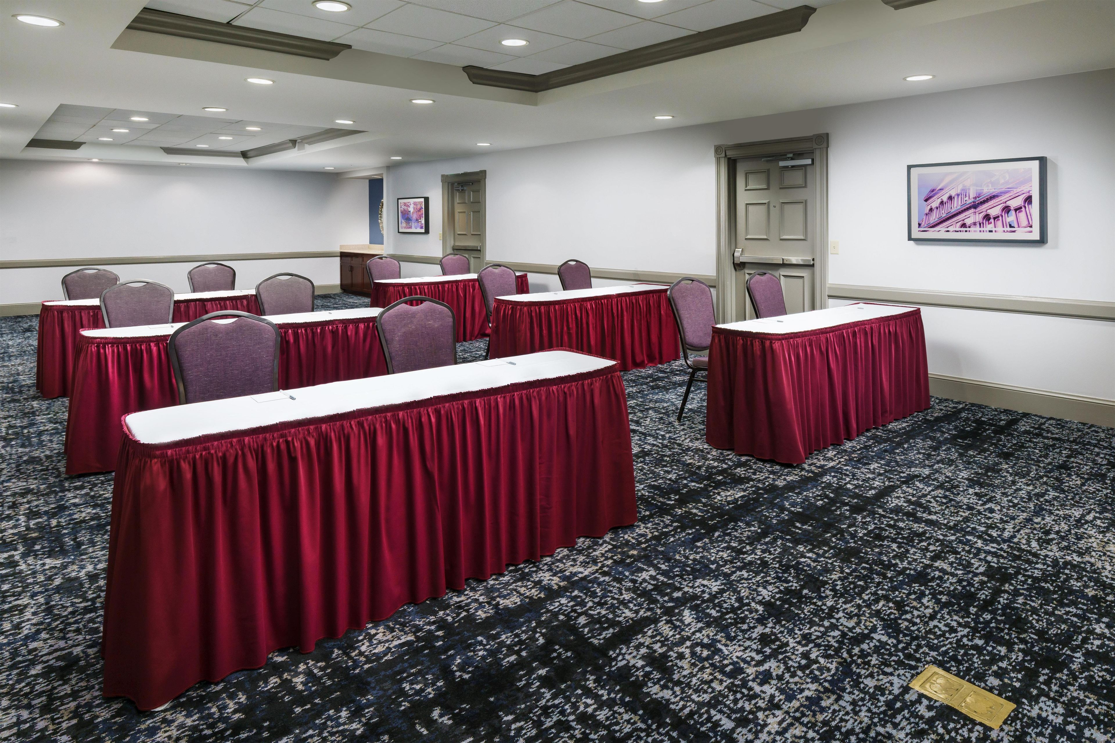 A conference room with tables and chairs, carpeted floor, and a door.