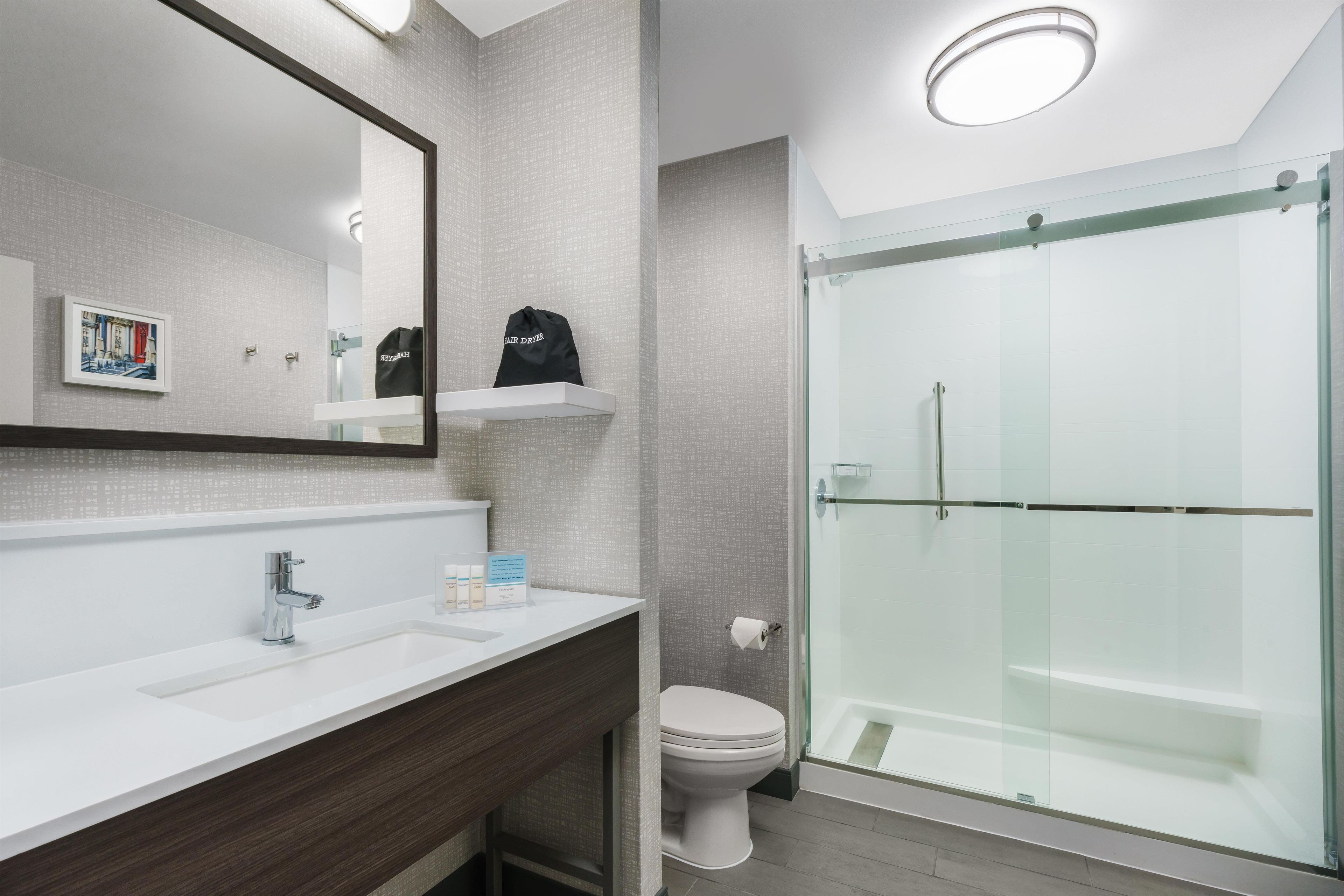 Un baño moderno con lavamanos blanco, un espejo, inodoro y ducha con mampara de vidrio.
