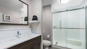 Un baño moderno con lavamanos blanco, un espejo, inodoro y ducha con mampara de vidrio.