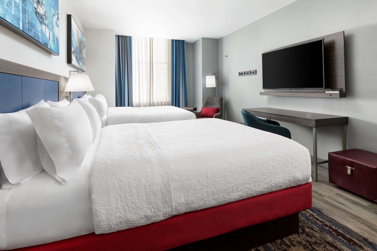 Ein Hotelzimmer mit zwei Betten, einem Schreibtisch, einem Fernseher und einem roten Koffer.