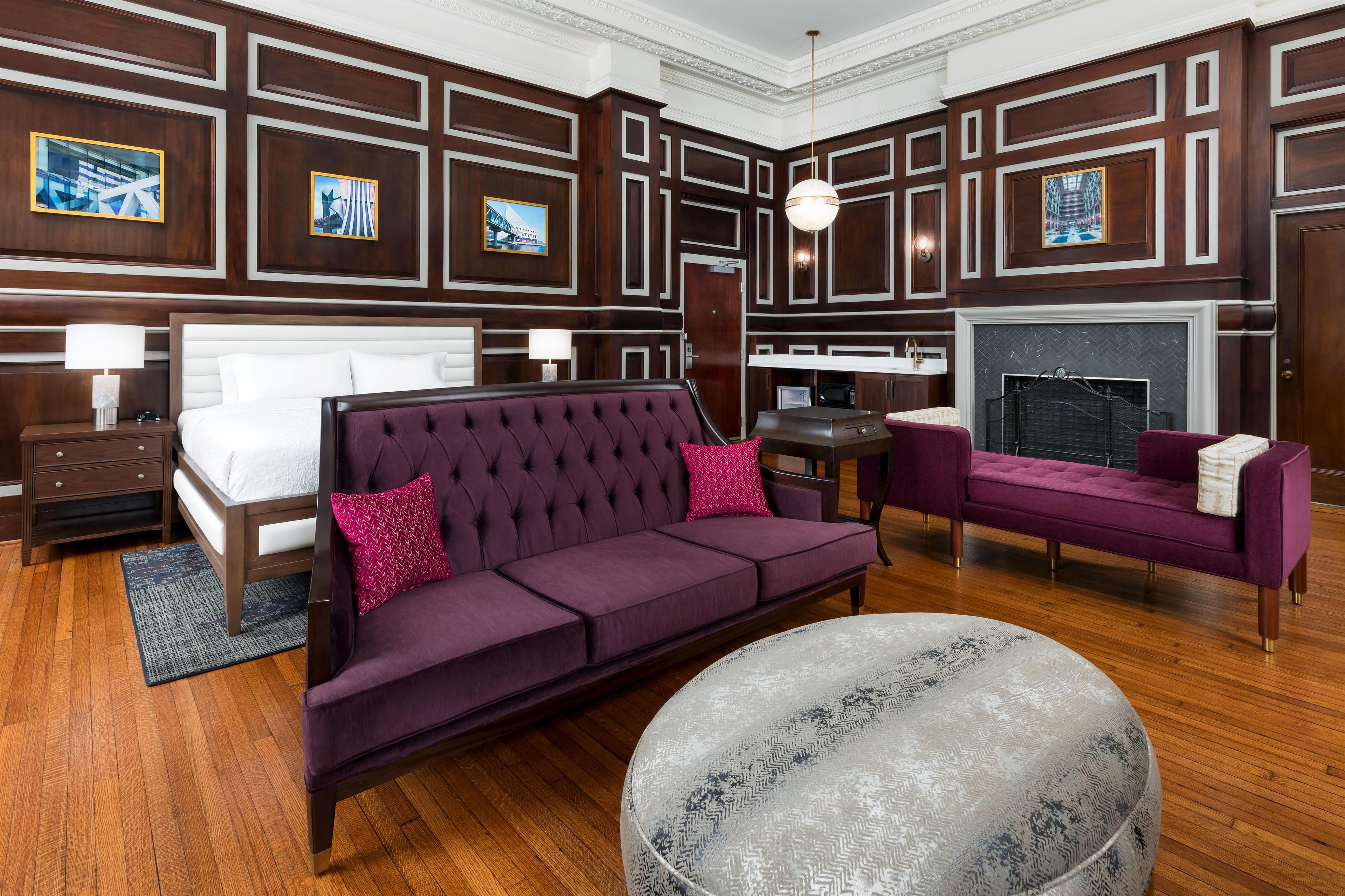 A hotel room with a large bed, a sofa, a small table, and a fireplace.