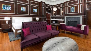 A hotel room with a large bed, a sofa, a small table, and a fireplace.