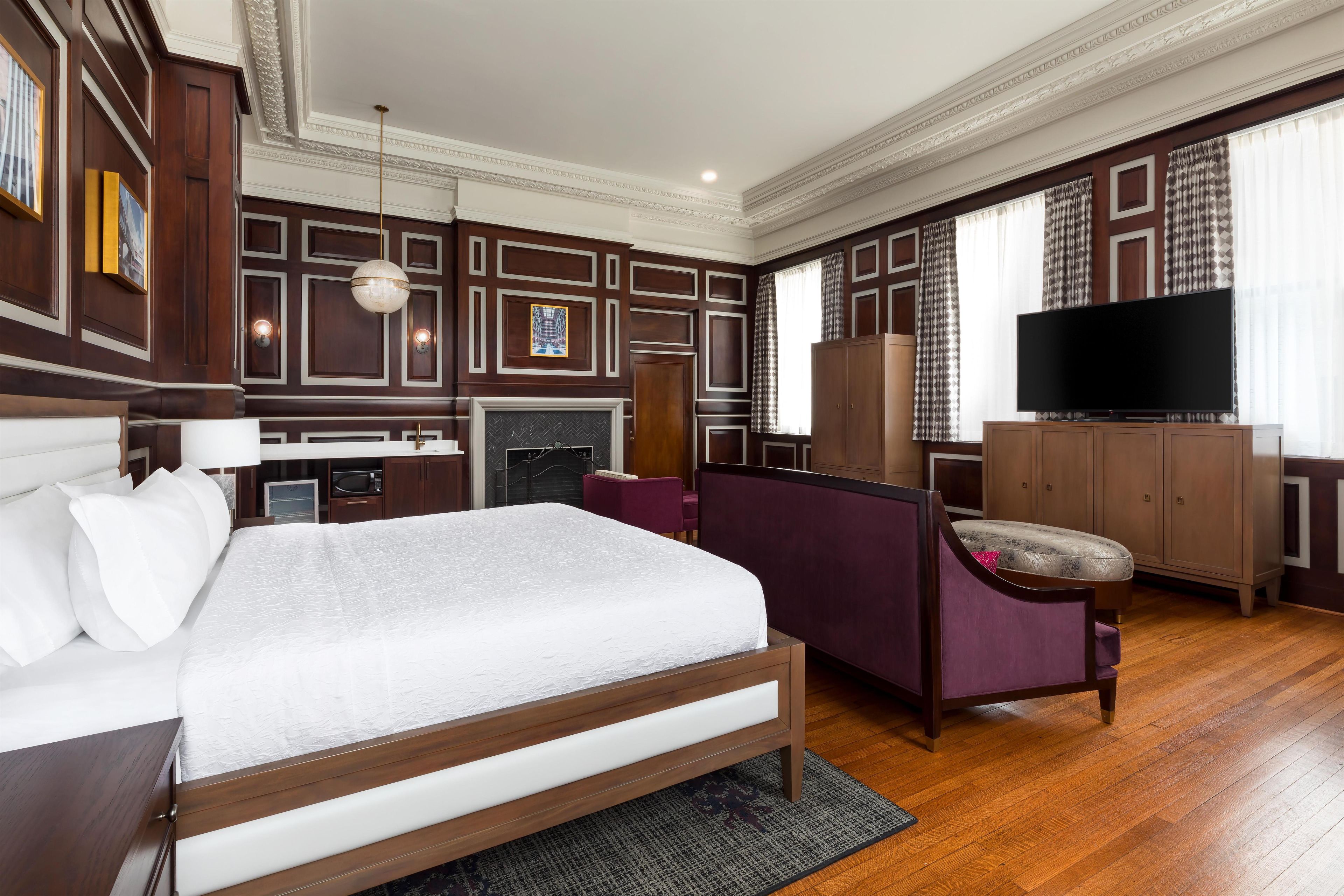 A hotel room with a large bed, a television, a desk, and a wardrobe.
