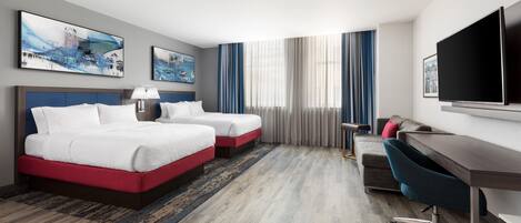 A hotel room with two beds, a desk, a chair, a TV, and artwork on the walls.