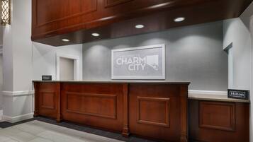 Un mostrador de recepción con un cartel que dice 'Welcome to Charm City', una placa de 'Hilton Honors' y un mapa enmarcado en la pared.
