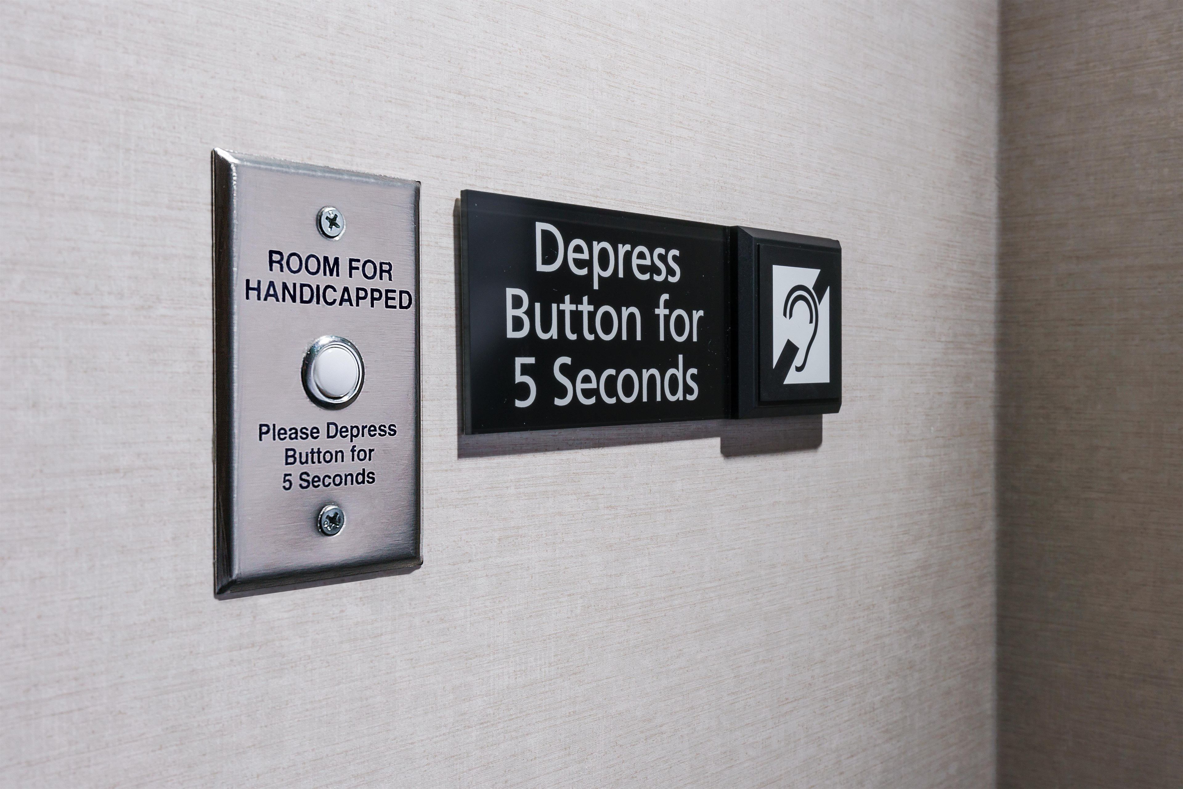 Schild mit Hinweis auf ein Zimmer für Menschen mit Behinderung und einem Druckknopf, der 5 Sekunden lang aktiviert wird.