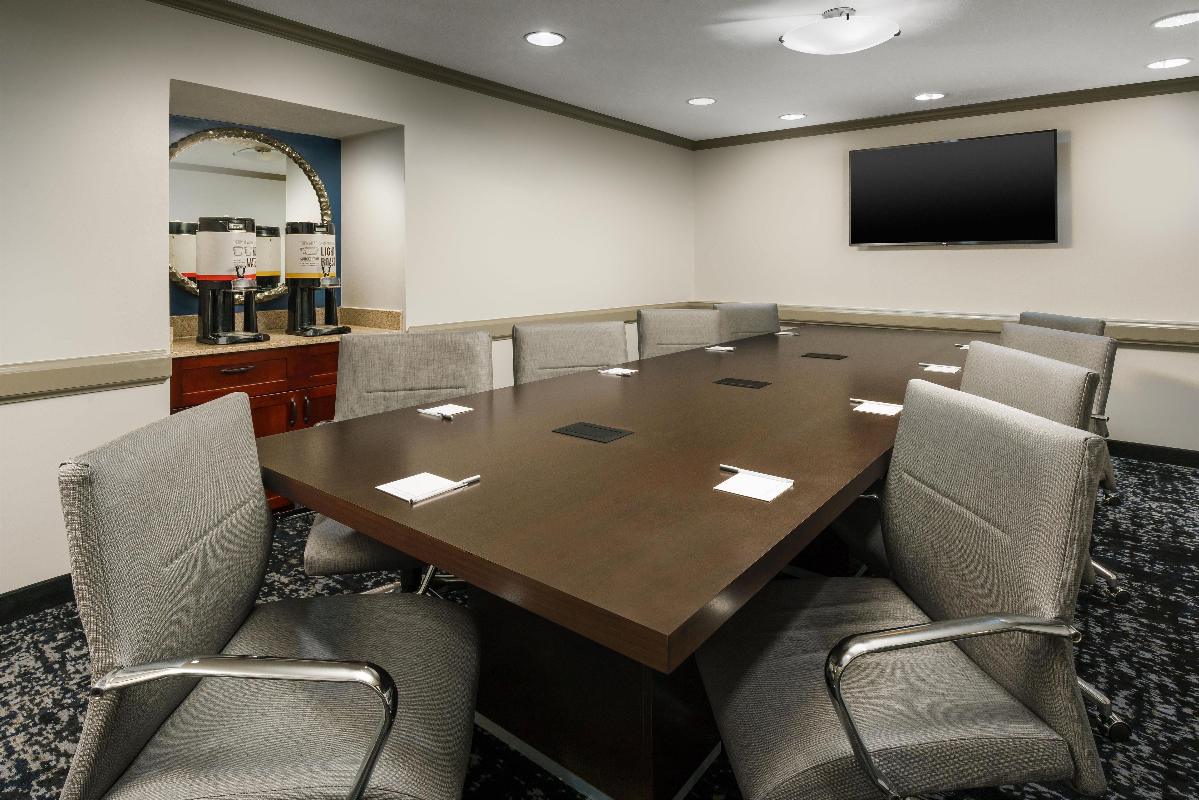 A conference room with a long table, six chairs, a flat-screen TV, and coffee makers.