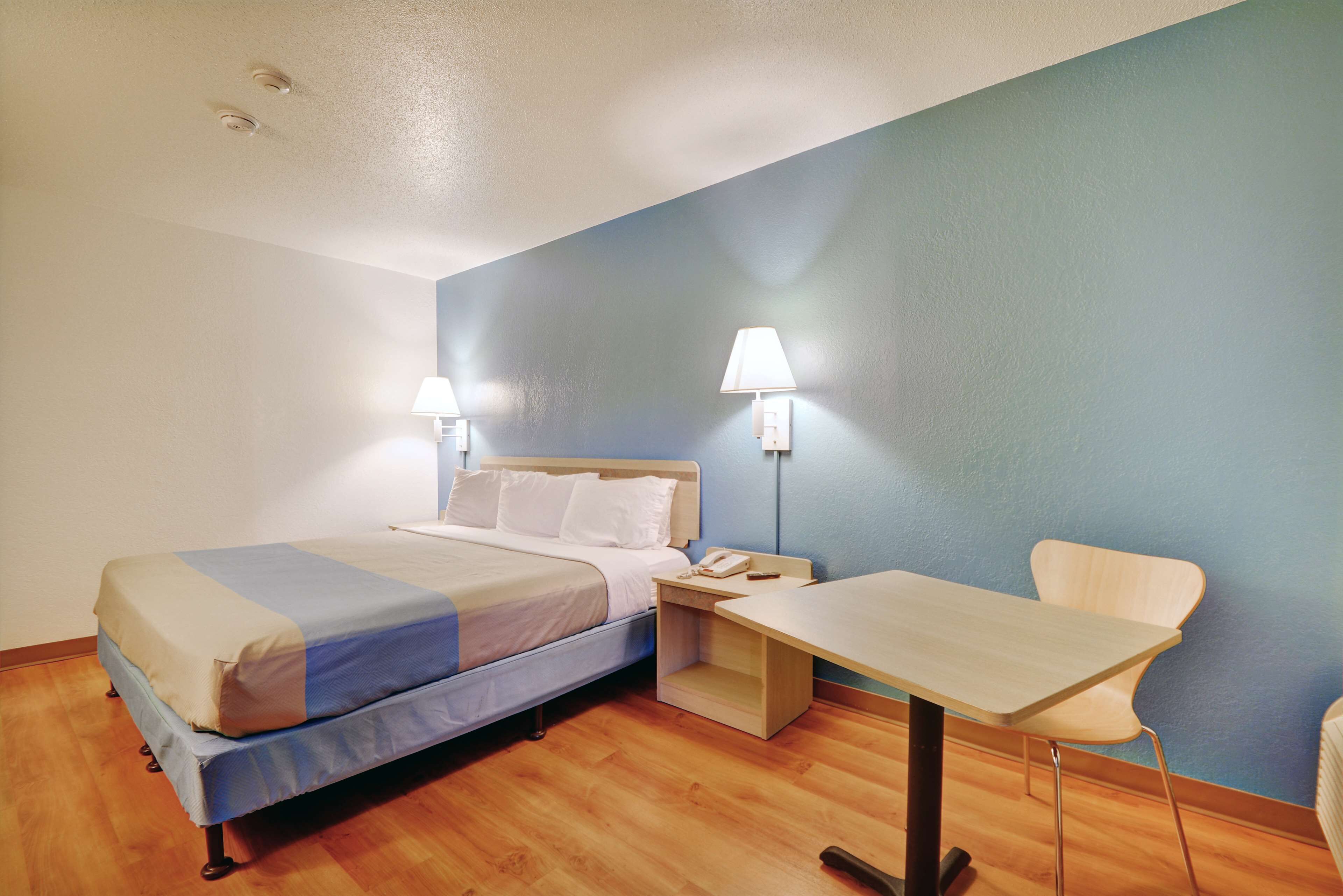 A hotel room with a bed, bedside table, lamp, chair, and a desk.