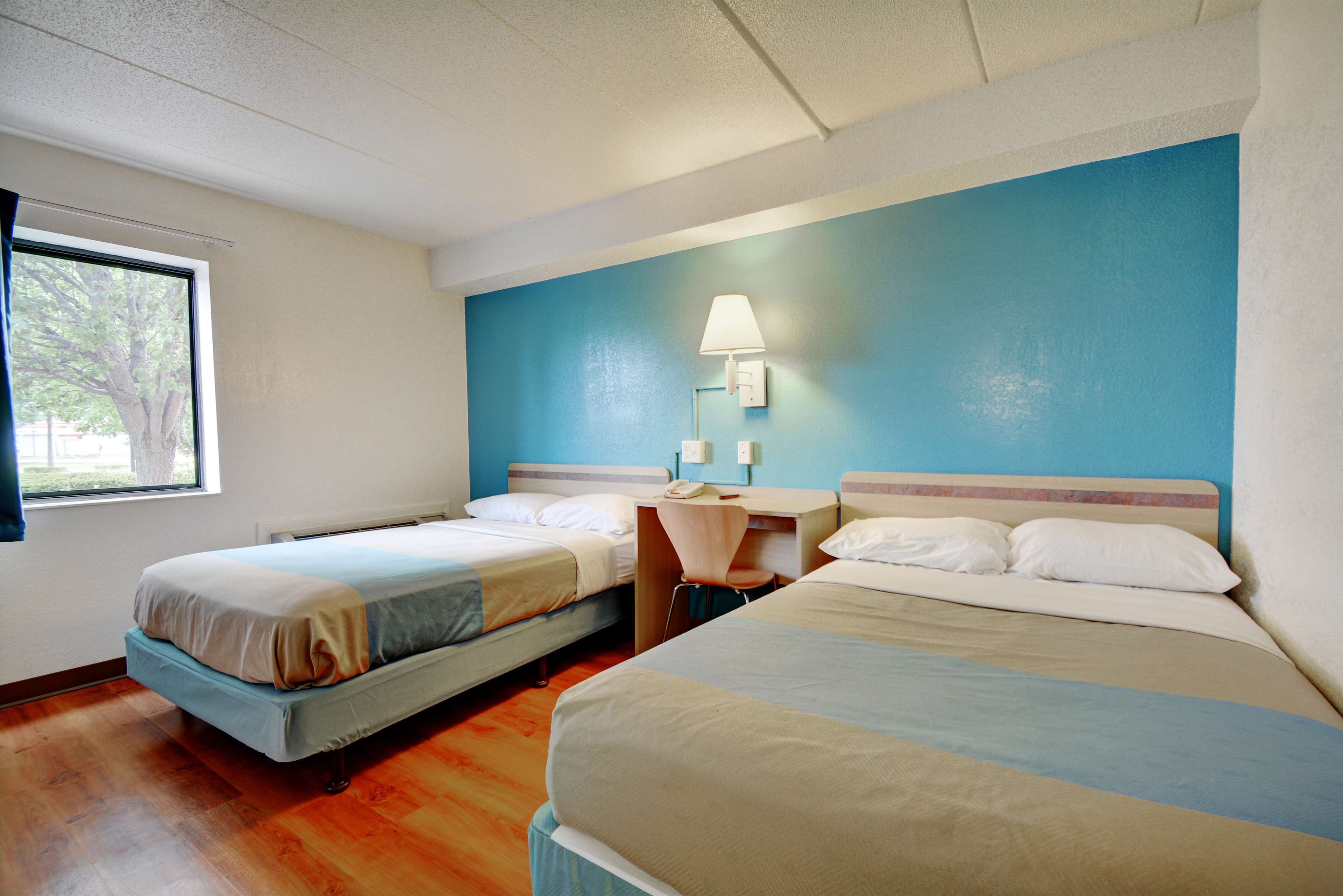 A hotel room with two beds, a desk, a chair, and a window.