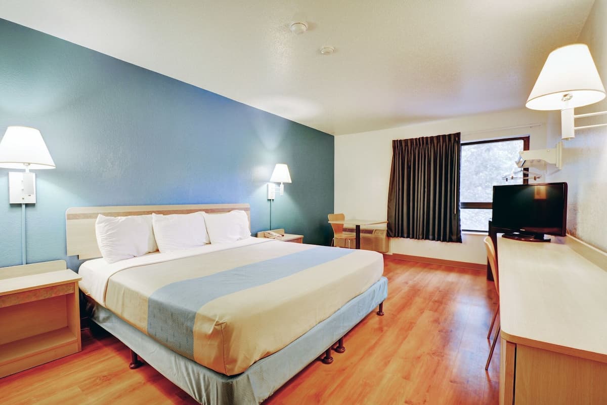A hotel room with a bed, bedside lamps, a desk, a television, and a window with curtains.