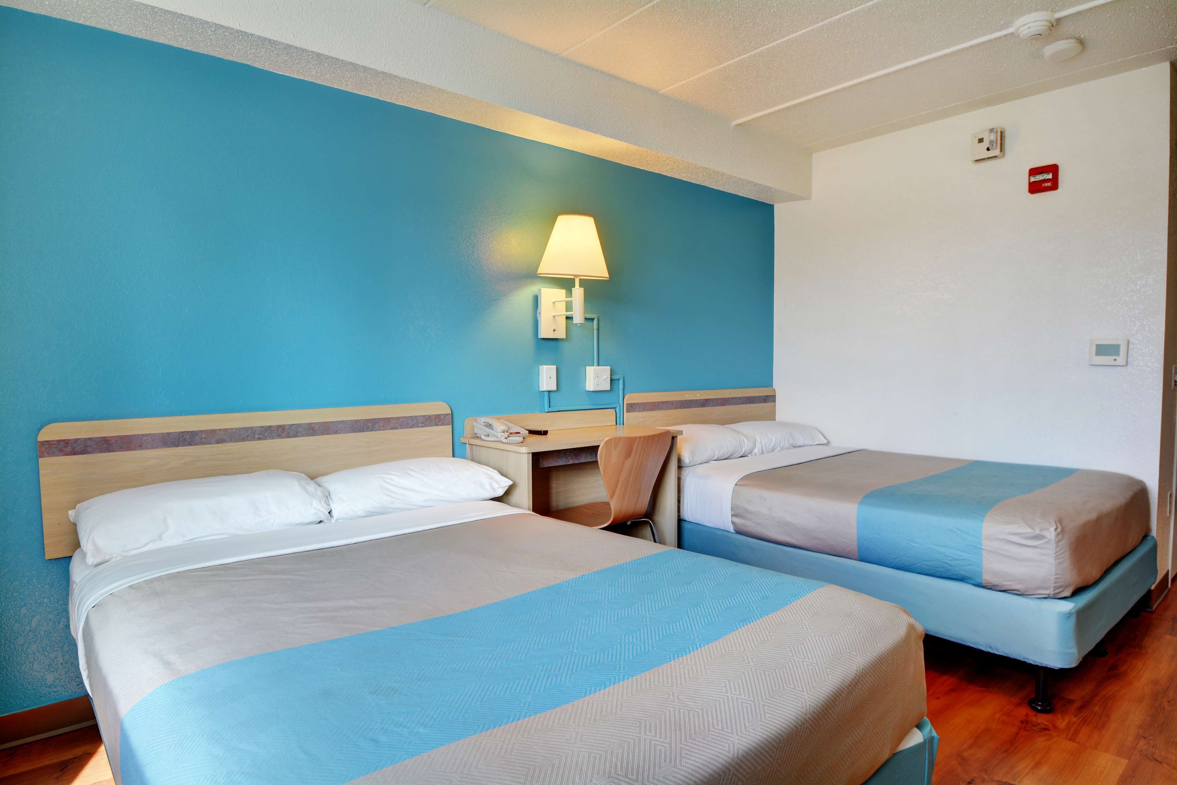 Una habitación de hotel con dos camas, un escritorio, una silla, una lámpara y un teléfono.