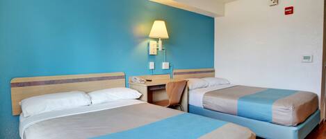 A hotel room with two beds, a desk, a chair, a lamp, and a phone.