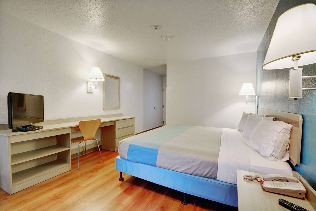A hotel room with a bed, a desk with a chair, a TV, and a phone.