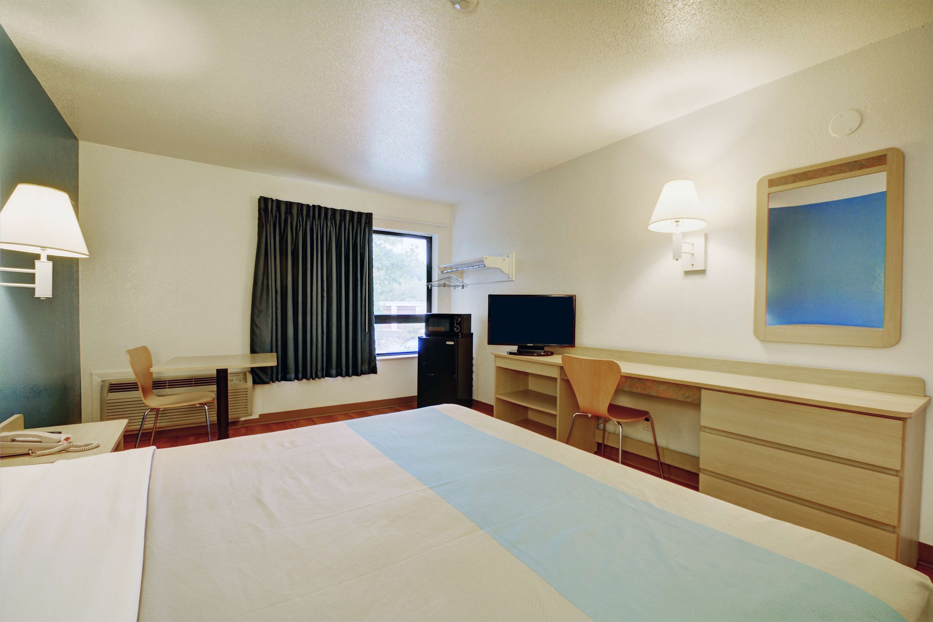 Habitación de hotel con cama, escritorio, silla, televisor y ventana con cortinas.