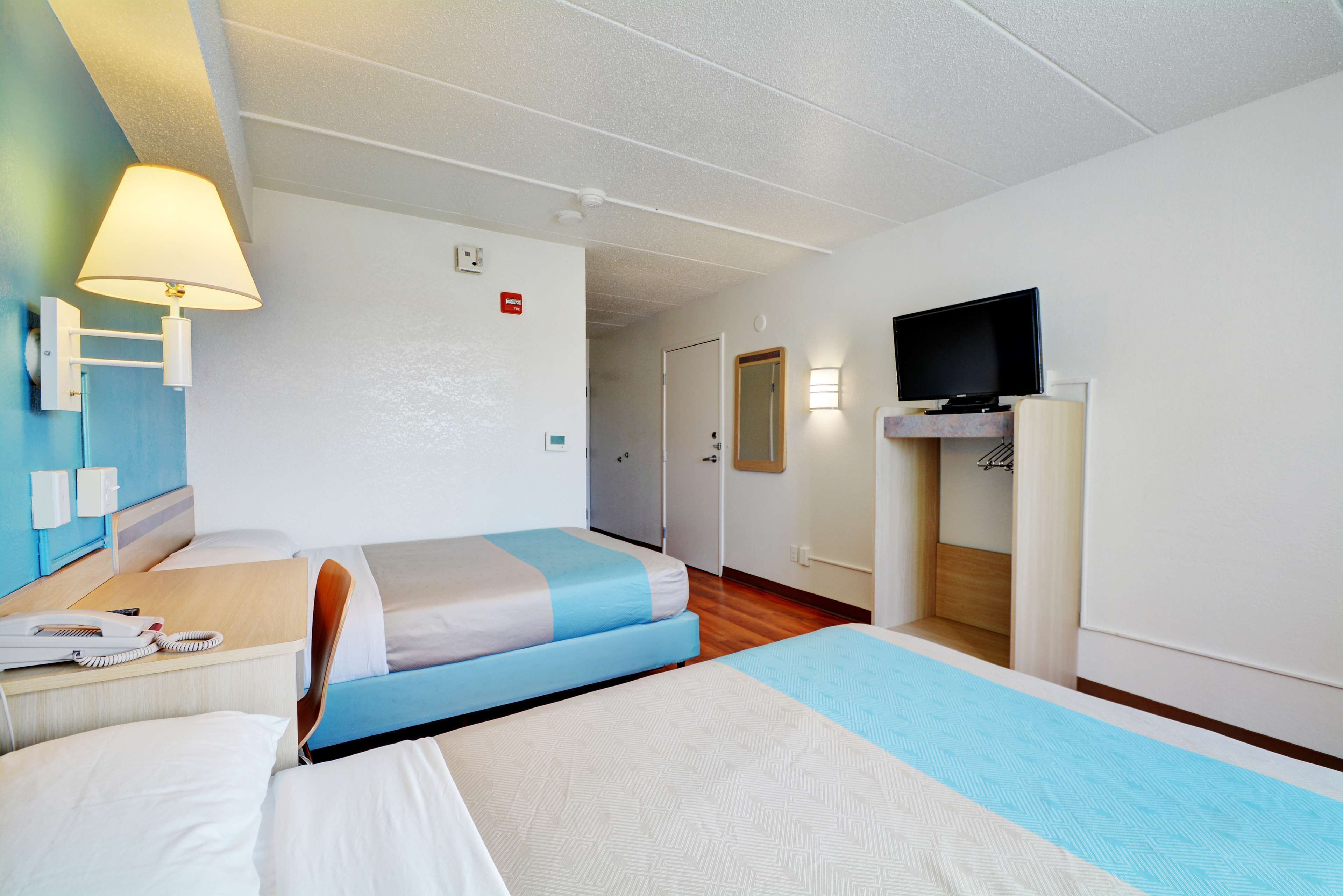 A hotel room with two beds, a desk with a telephone, a television on a stand, and a bathroom visible through an open door.