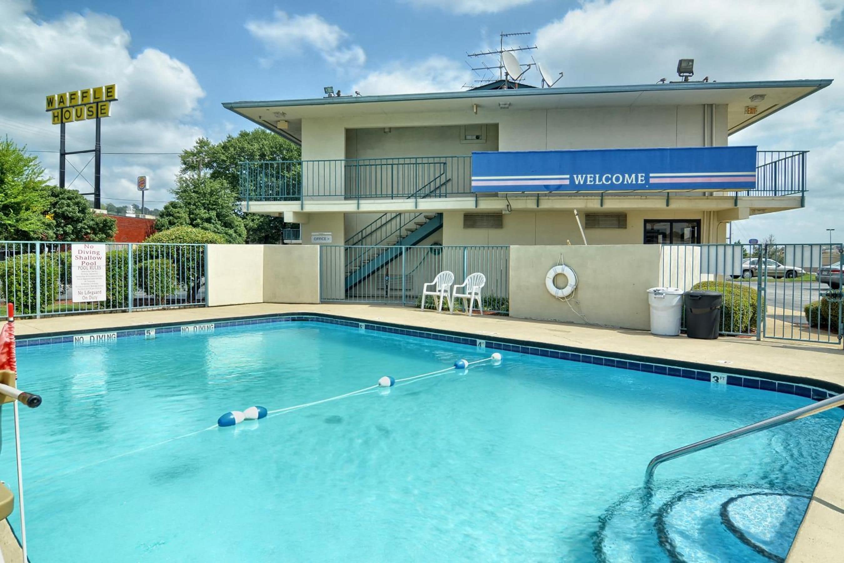 A swimming pool with a 'Welcome' sign, a lifeguard stand, and a no diving sign.