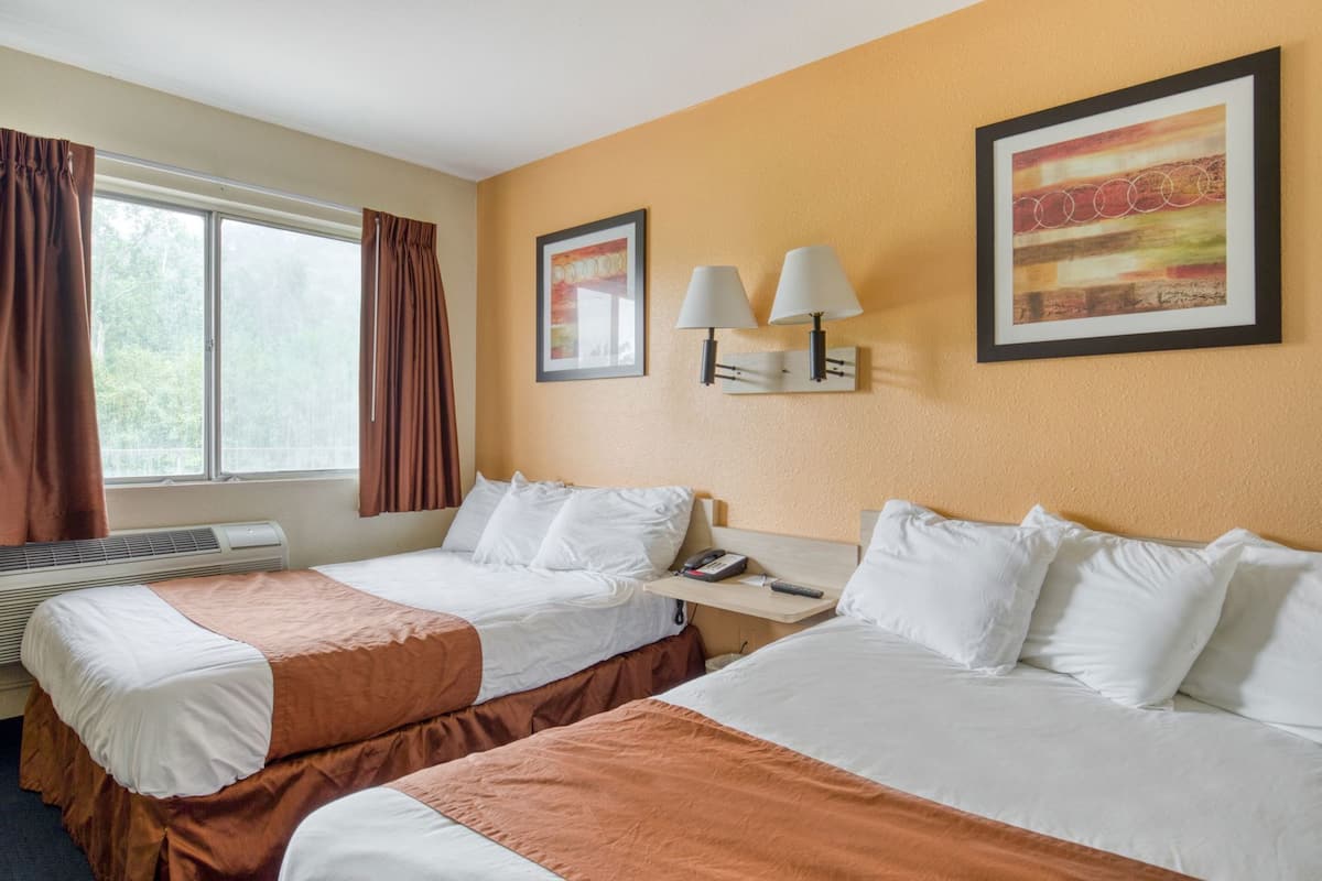 A hotel room with two beds, a heater, a window with curtains, and wall-mounted lamps.