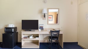 Une chambre d’hôtel équipée d’un lit, d’un bureau avec un ordinateur, d’une télévision, d’un four à micro-ondes, d’une chaise et d’un petit réfrigérateur.