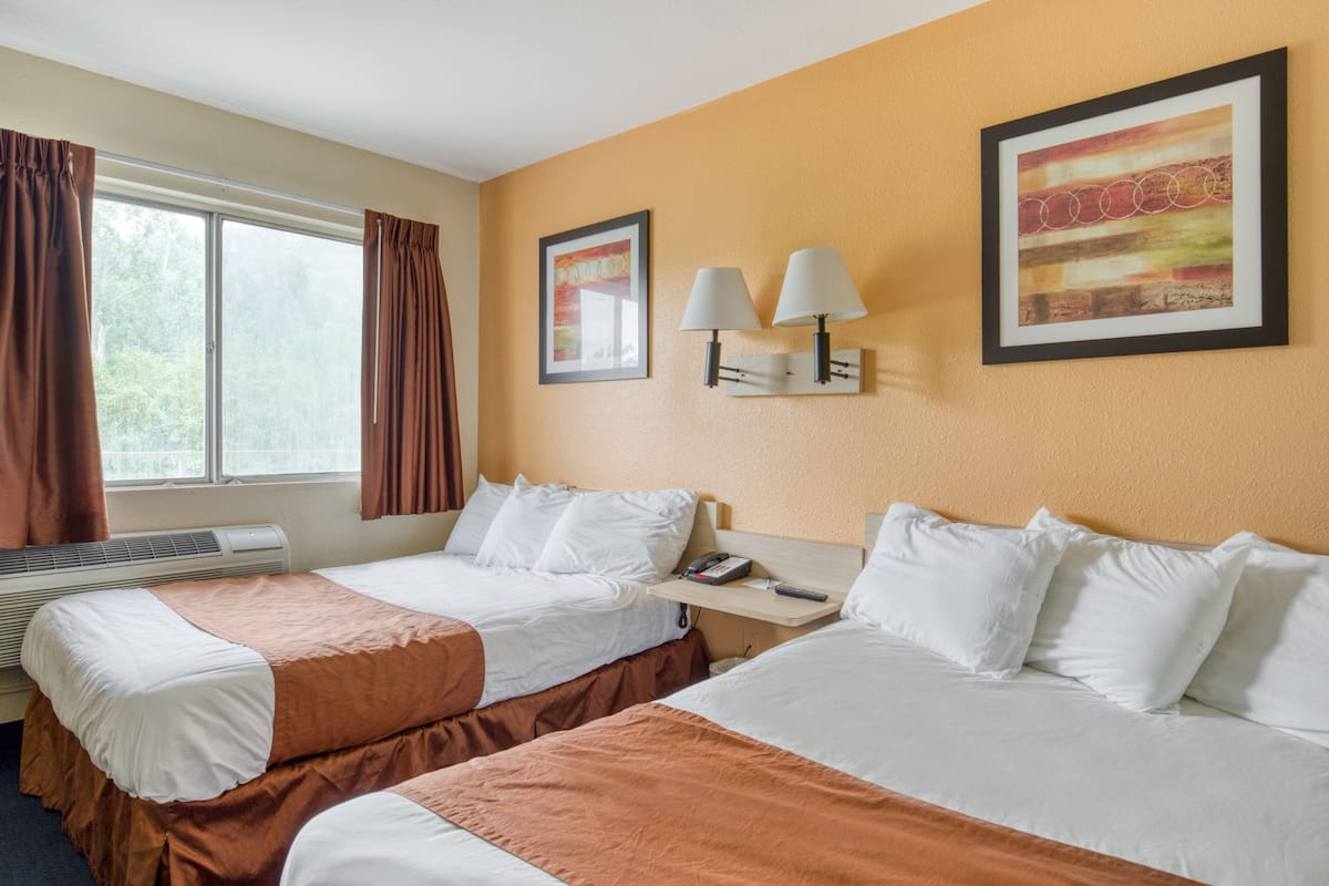 A hotel room with two beds, a window with curtains, a wall-mounted lamp, and a framed picture.