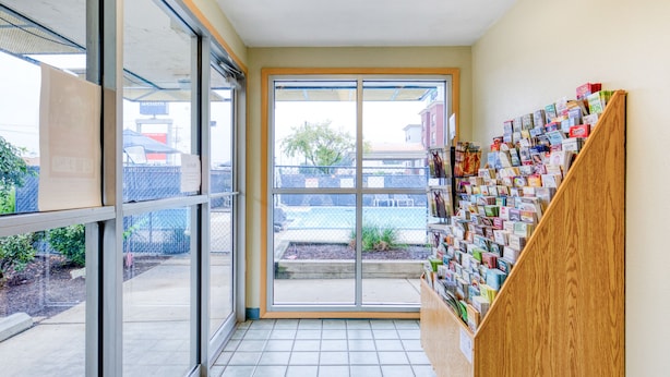 Un couloir avec une porte vitrée donnant sur l’extérieur, un escalier en bois et un mur où sont accrochées diverses cartes ou brochures.