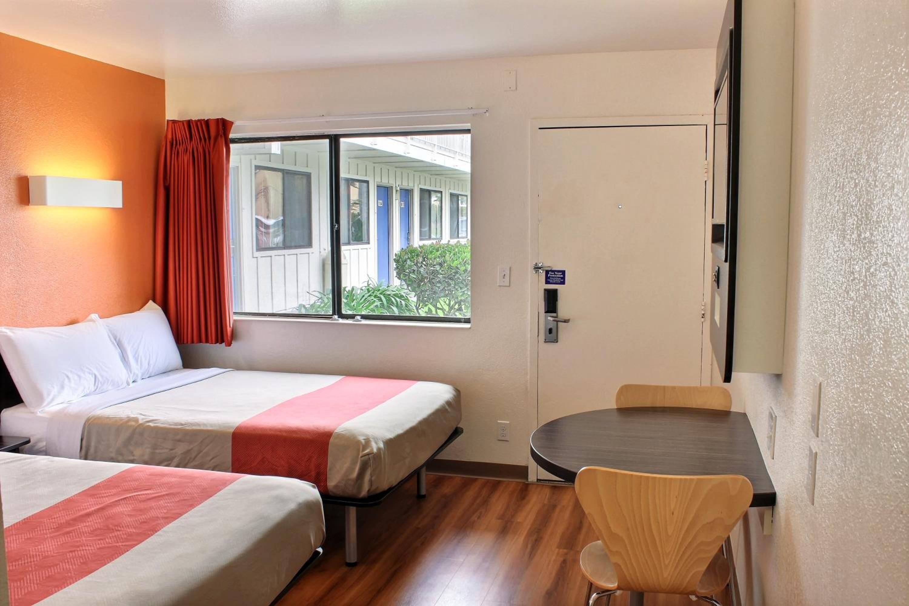 A hotel room with two beds, a small table, and a chair.